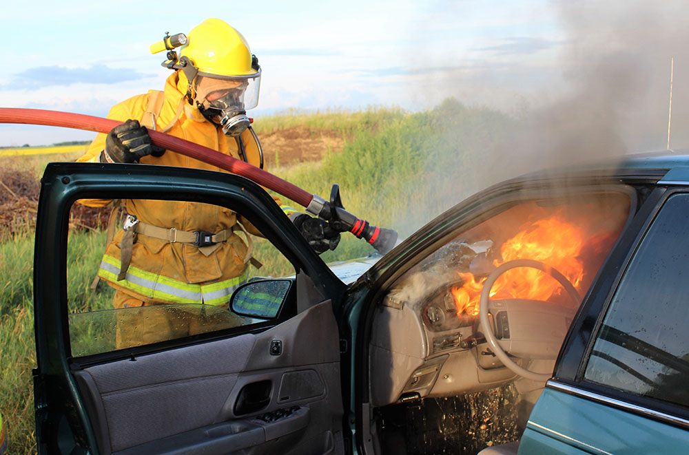 Fire fighter holding hose extinguishing fire in car