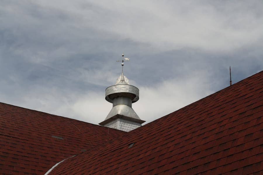 Close up of silver weather vane on red shingled barn roof